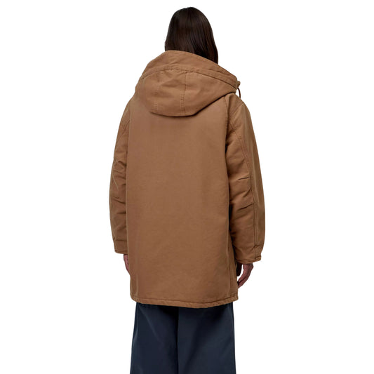 Parka Carhartt WIP Boreal em WIP H Brown — modelo masculino de costas, corpo inteiro, lona Dearborn castanha, capuz volumoso com costuras traseiras visíveis, corte amplo abaixo da anca, calças largas azul-marinho, fundo branco.