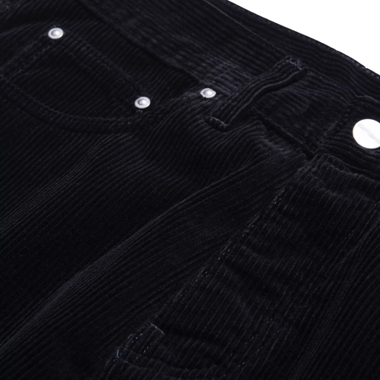 alças Carhartt WIP Newel Pant em Black — detalhe da cintura frontal em close, bombazina Coventry de oito nervuras preta, fecho de correr com puxador prateado, bolsos frontais com rebites prateados e aba de micro-bolso visível, textura canelada larga em destaque, fundo branco.