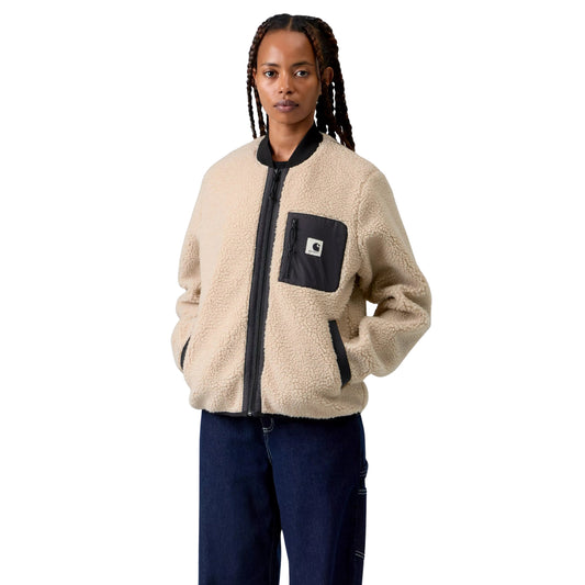 Casaco polar Carhartt WIP W' Janet Liner em Fleur De Sel / Black — modelo feminino de frente, meio corpo, tranças longas, casaco fechado, pile de poliéster texturado bege areia Fleur de Sel, gola canelada preta, fecho de correr frontal preto, bolso de peito esquerdo em tafetá de nylon preto com etiqueta Square Label Carhartt e puxador de fecho preto, bolsos laterais com debrum preto e mãos nos bolsos, calças wide-leg denim azul-escuro, fundo branco.
