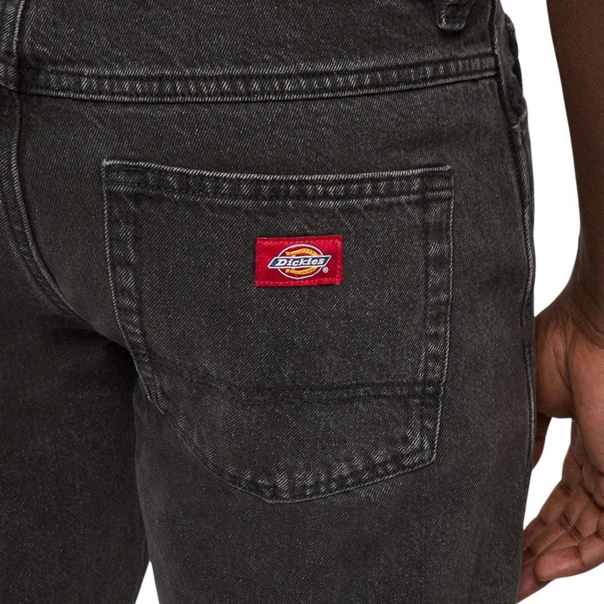 Pormenor do bolso traseiro das calças Dickies 983 Black Wash, com etiqueta vermelha da marca e textura da ganga lavada.