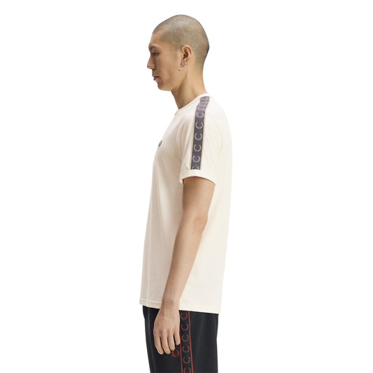 T-shirt de manga curta Fred Perry Contrast Tape Ringer em Ecru — modelo de perfil, t-shirt ecru de corte regular, fita desportiva azul-marinho com padrão de coroas de louros desde o ombro até à manga, colarinho redondo e punho dobrado, fundo branco.