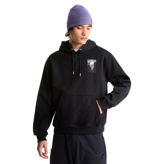 Hoodie The North Face Apex '75 Collage Relaxed em TNF Black — modelo masculino de frente, gorro TNF lilás/roxo, calças cargo azul-marinho escuro, mão no bolso canguru, logo TNF Apex '75 Collage em caixa em serigrafia no peito esquerdo visível, corte relaxed, fundo branco.