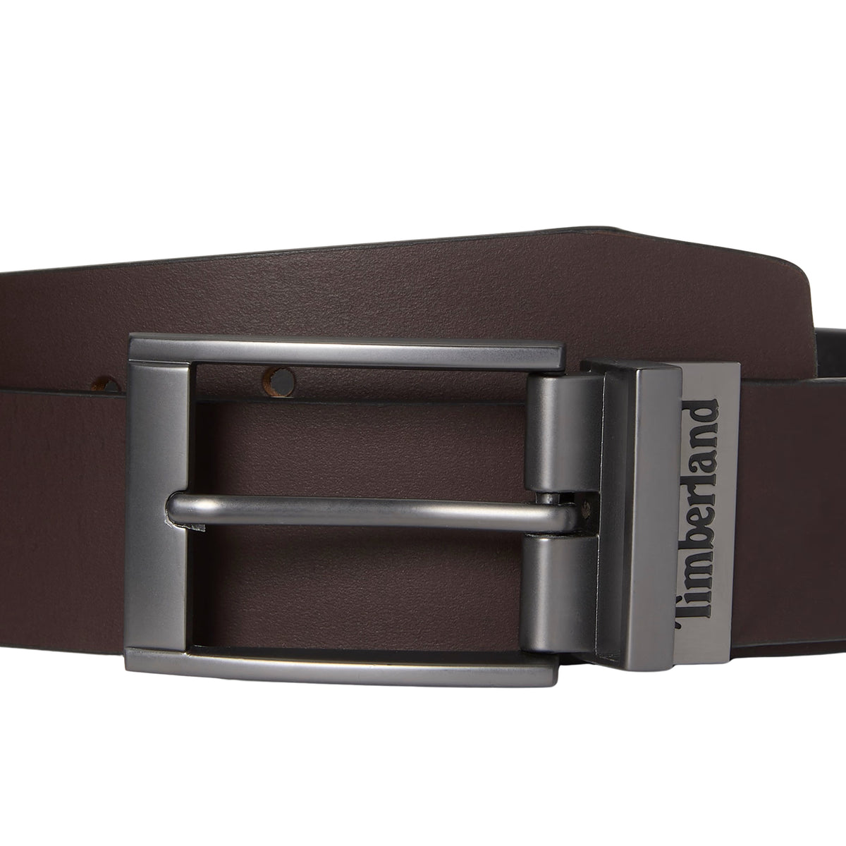 Cinto reversível Timberland Bartley para homem em Castanho/Preto — close-up da fivela reversível em cinza fosco com presilha em metal e logo Timberland gravado na lateral, correia em pele castanha lisa, fundo branco.
