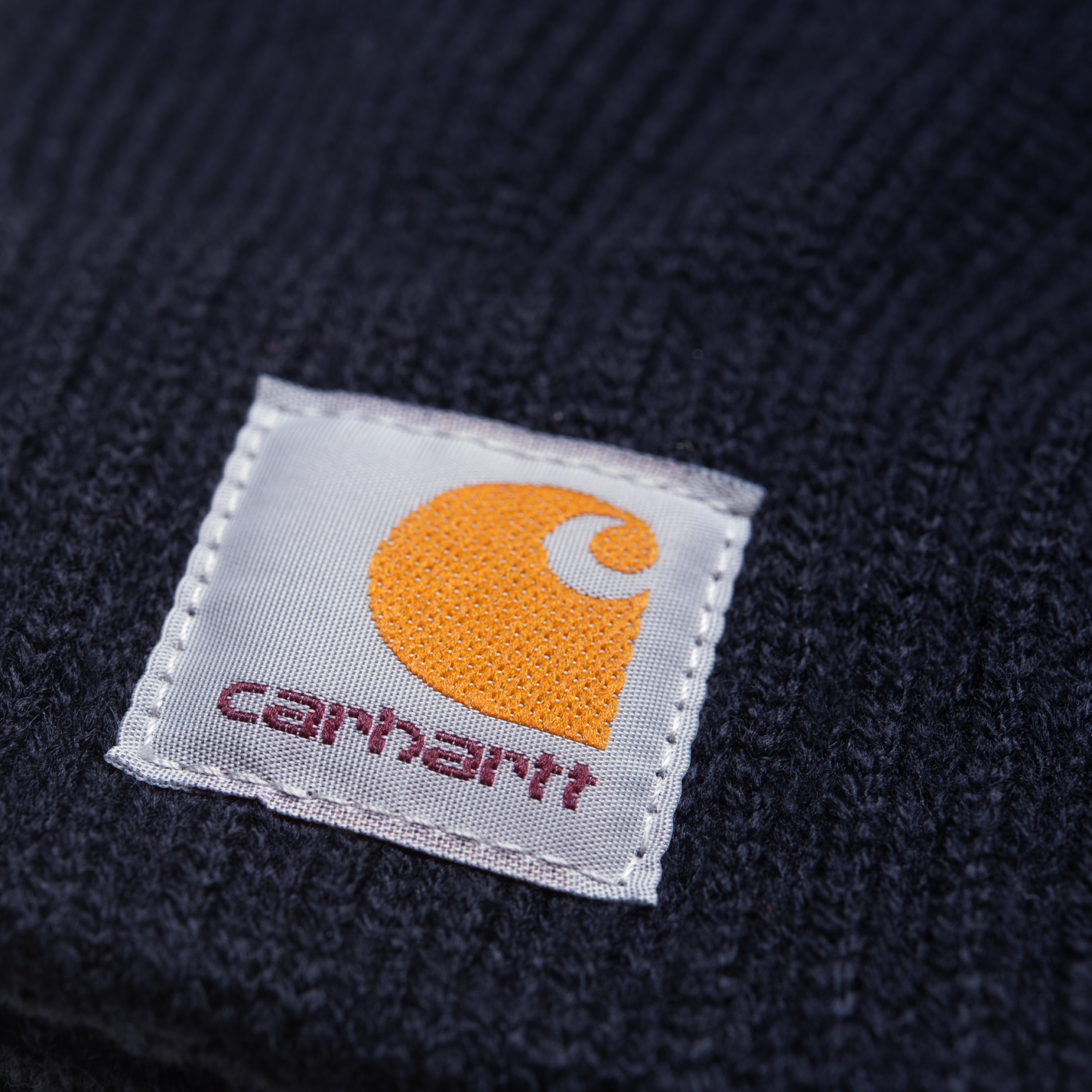 Carhartt WIP Watch Gloves em Dark Navy. Foto de detalhe do logotipo.