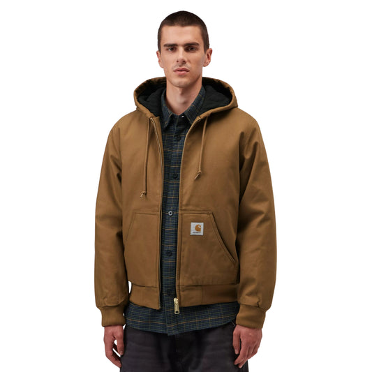 Casaco com carapuço Carhartt WIP Active em Hamilton Brown, vista frontal em plano médio no modelo, usado aberto sobre uma camisa escura de padrão xadrez, com fecho metálico, cordões e etiqueta quadrada no bolso.