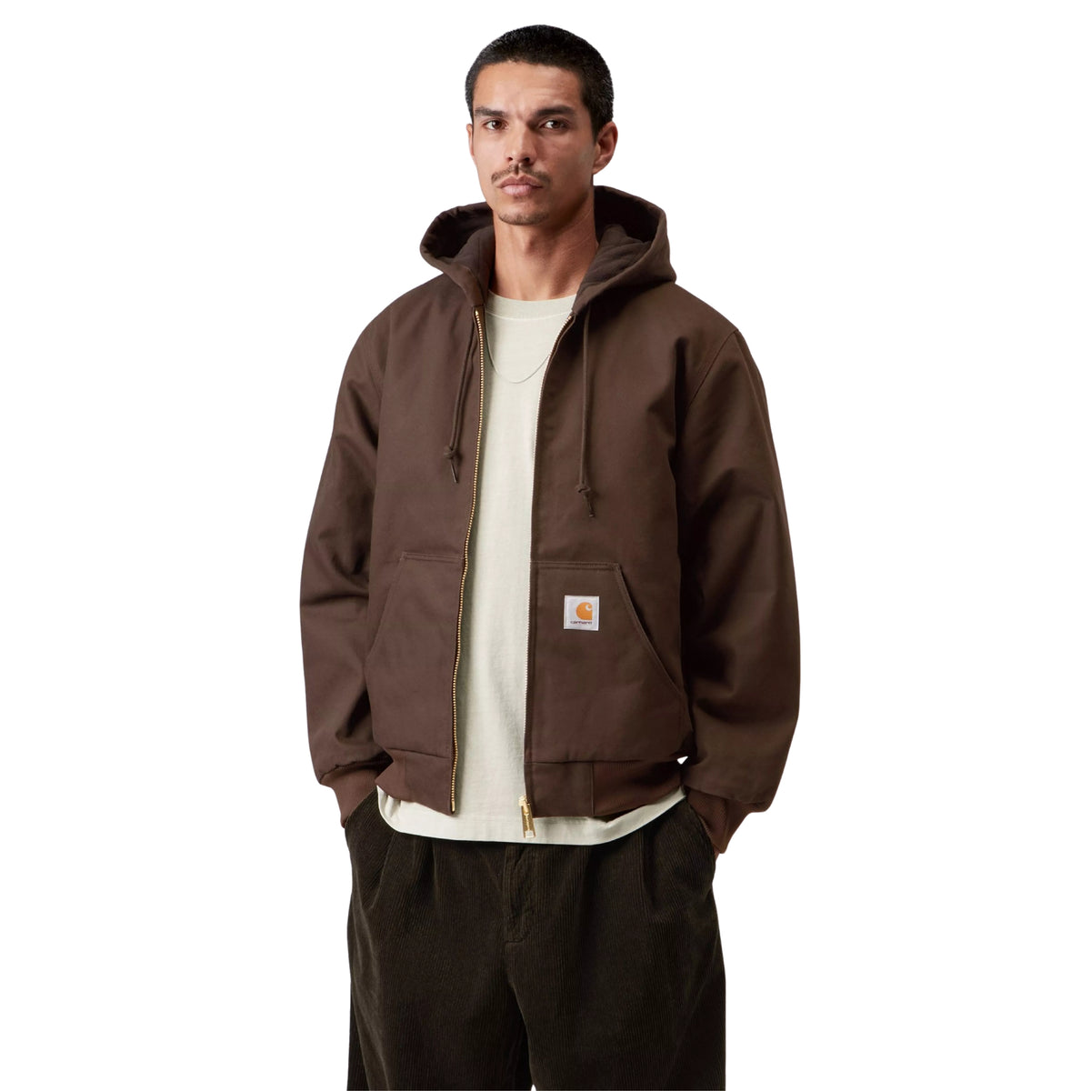 Casaco com carapuço Carhartt WIP Active em Tobacco Rigid, vista frontal em plano médio no modelo, usado aberto sobre uma t-shirt clara, com cordões, fecho metálico e etiqueta quadrada no bolso.