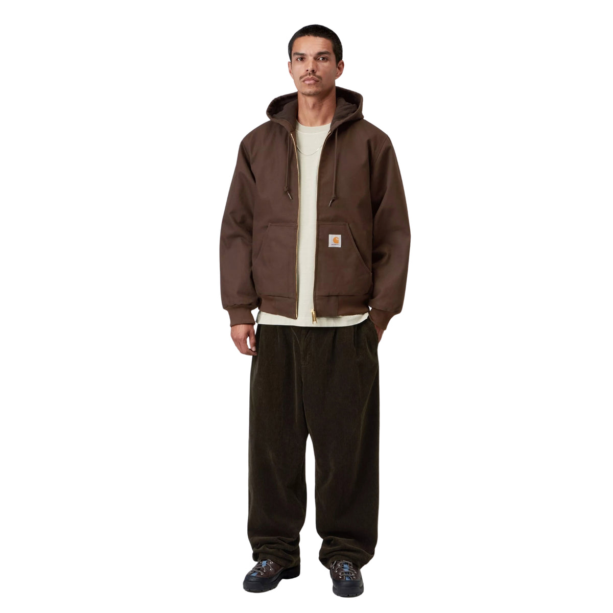 Casaco com carapuço Carhartt WIP Active em Tobacco Rigid, vista frontal de corpo inteiro no modelo, usado aberto sobre uma t-shirt clara, com calças largas escuras e calçado preto.