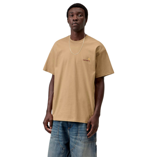 T-shirt Carhartt WIP S/S American Script em Dusty H Brown — modelo a usar a peça de frente, meio corpo superior, decote redondo, logótipo C amarelo-dourado com texto carhartt castanho em tom-sobre-tom no peito esquerdo, malha de algodão orgânico bege-camel arenoso, fundo branco.