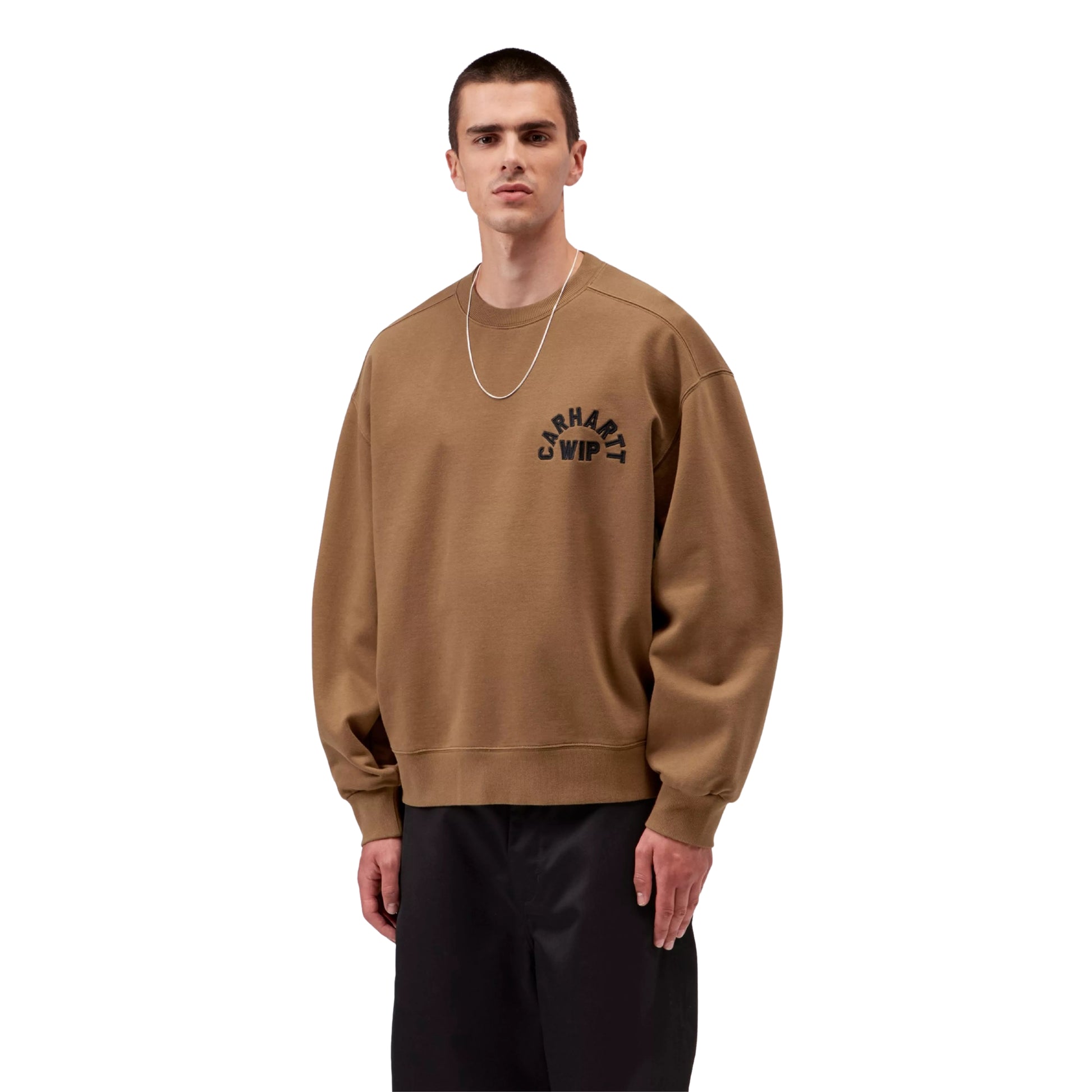 Sweat para homem Carhartt WIP Arch Script em WIP H Brown / Black Stone Washed — modelo masculino de frente, meio corpo, calças largas pretas, colar fino dourado, bordado em arco "Carhartt WIP" em preto no peito esquerdo, corte balloon e decote redondo visíveis, fundo branco.