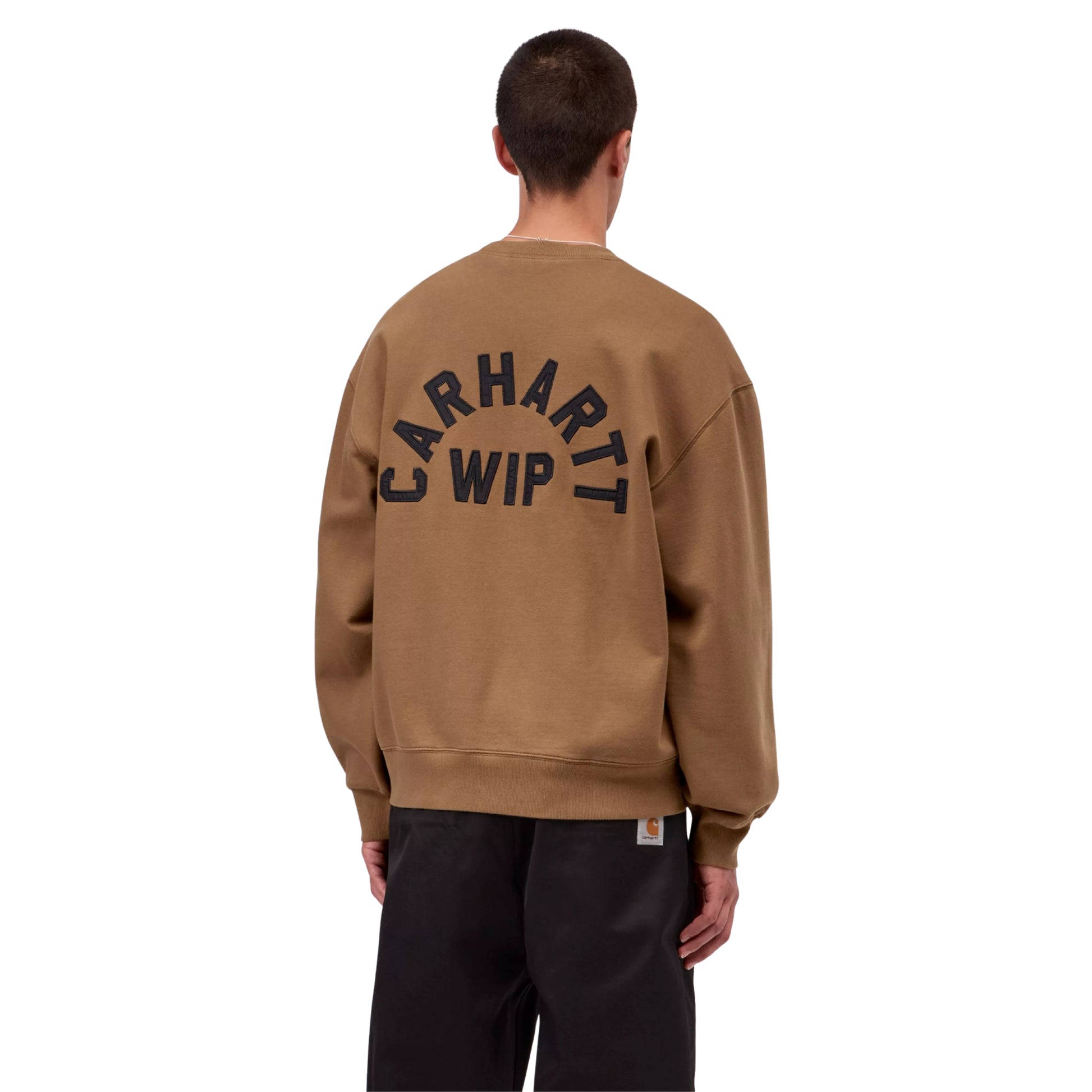 Sweat para homem Carhartt WIP Arch Script em WIP H Brown / Black Stone Washed — modelo masculino de costas, meio corpo, calças largas pretas, bordado em arco "Carhartt WIP" em preto nas costas sobre tom WIP H Brown, costuras dos ombros caídas e punhos canelados visíveis, fundo branco.