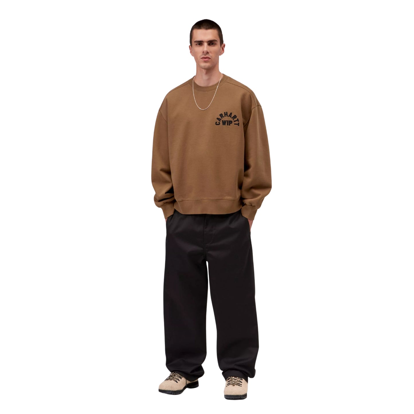 Sweat para homem Carhartt WIP Arch Script em WIP H Brown / Black Stone Washed — modelo masculino de frente, corpo inteiro, calças largas pretas, botas de caminhada bege, mãos nos bolsos, bordado em arco "Carhartt WIP" em preto no peito esquerdo e corte balloon com bainha canelada visíveis, fundo branco.