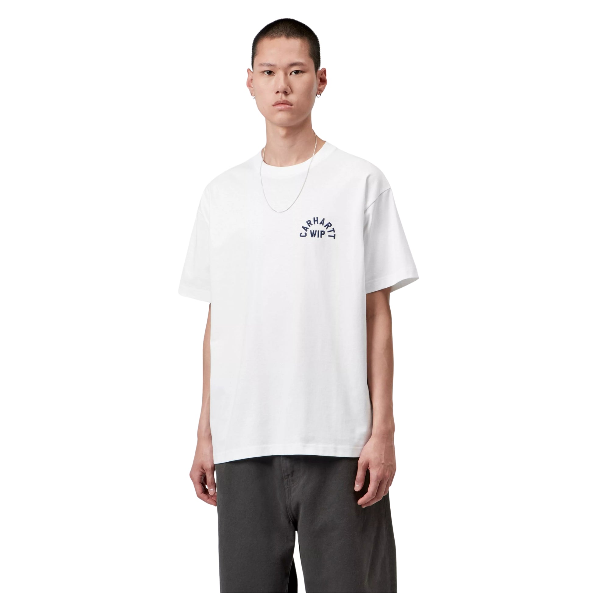 T-shirt Carhartt WIP S/S Arch Script em White / Dark Navy — modelo masculino de frente, meio corpo superior, cabelo curto, fio prateado ao pescoço, brinco prateado, t-shirt branca de algodão orgânico com corte solto e bordado tipográfico "CARHARTT WIP" em arco azul-marinho escuro no peito esquerdo, calças wide-leg cinzento-escuras, fundo branco.