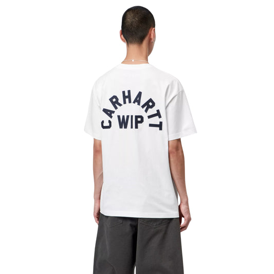 T-shirt Carhartt WIP S/S Arch Script em White / Dark Navy — modelo masculino de costas, meio corpo superior, cabelo curto, fio prateado ao pescoço, t-shirt branca de algodão orgânico com apliques tipográficos "CARHARTT WIP" em arco azul-marinho escuro nas costas, letras em relevo costuradas em jersey, calças wide-leg cinzento-escuras, fundo branco.