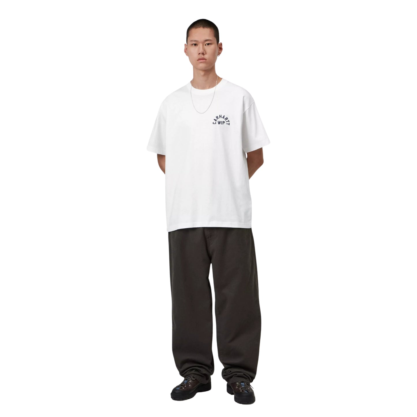 T-shirt Carhartt WIP S/S Arch Script em White / Dark Navy — modelo masculino de corpo inteiro, cabelo curto, fio prateado ao pescoço, t-shirt branca de algodão orgânico com corte solto e bordado "CARHARTT WIP" em arco no peito esquerdo, mãos nos bolsos, calças wide-leg castanho-escuras, sapatilhas chunky pretas, fundo branco.