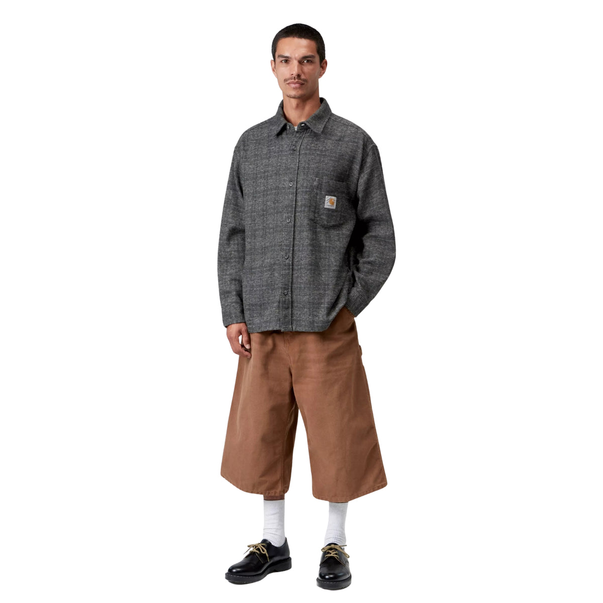Camisa de manga comprida Carhartt WIP L/S Bagley em Bagley Check Preto — modelo masculino de corpo inteiro, frente, xadrez Bagley Check cinzento antracite, bolso de peito com Square Label Carhartt WIP dourada, corte loose, bermudas largas camel abaixo do joelho, meias brancas e sapatos derby pretos, fundo branco.