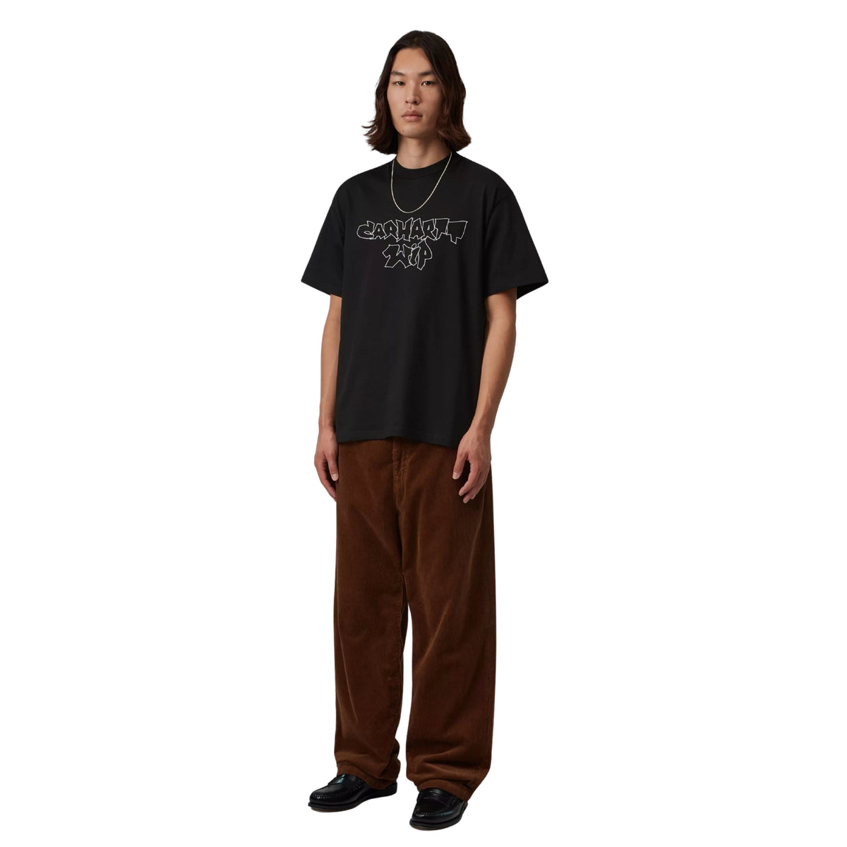 Modelo de corpo inteiro com t-shirt Carhartt WIP Blinkerfluid preta, gráfico no peito, calças castanhas de bombazina e sapatos pretos.