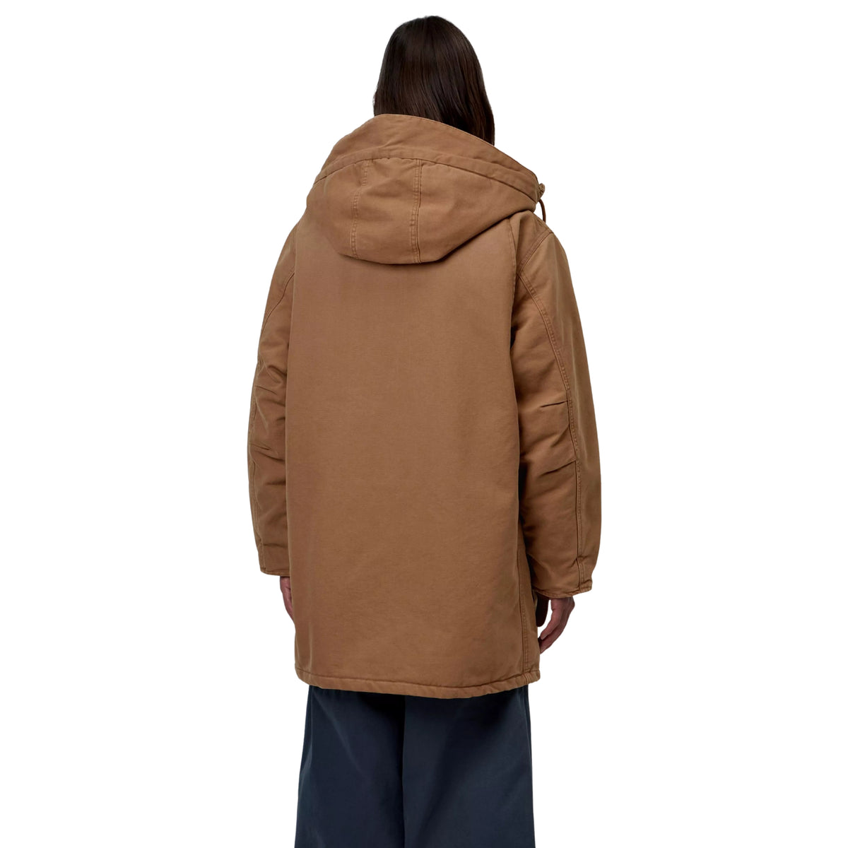 Parka Carhartt WIP Boreal em WIP H Brown — modelo masculino de costas, corpo inteiro, lona Dearborn castanha, capuz volumoso com costuras traseiras visíveis, corte amplo abaixo da anca, calças largas azul-marinho, fundo branco.