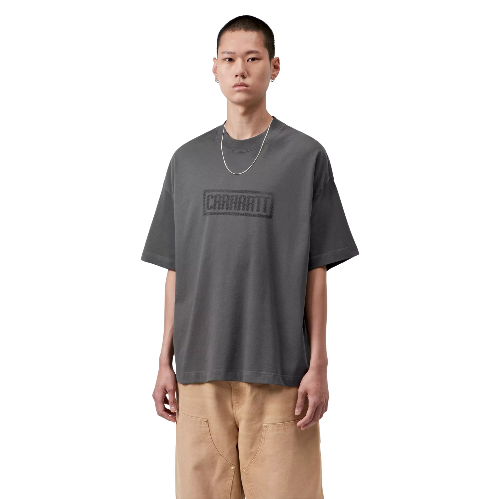 T-shirt Carhartt WIP S/S Bricky Man em Soot Stone Dyed — modelo masculino de frente, meio corpo, cabelo curto, brinco pequeno, fio de prata fino ao pescoço, gráfico Bricky Man impresso no peito: logotipo "Carhartt" em caixa retangular cinzento escuro tom-sobre-tom, malha de algodão orgânico cinzento Soot stone-dyed, calças cargo wide-leg bege Carhartt WIP, fundo branco.
