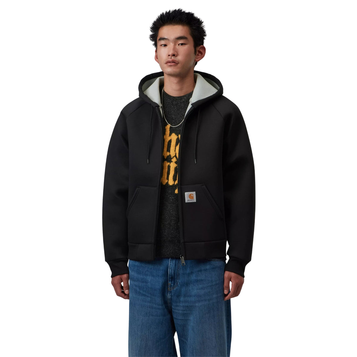 Casaco com carapuço Carhartt WIP Car-Lux em Black/Grey, vista frontal em plano médio no modelo, usado aberto sobre uma t-shirt escura com estampado amarelo, com interior cinzento do carapuço e etiqueta quadrada no bolso.