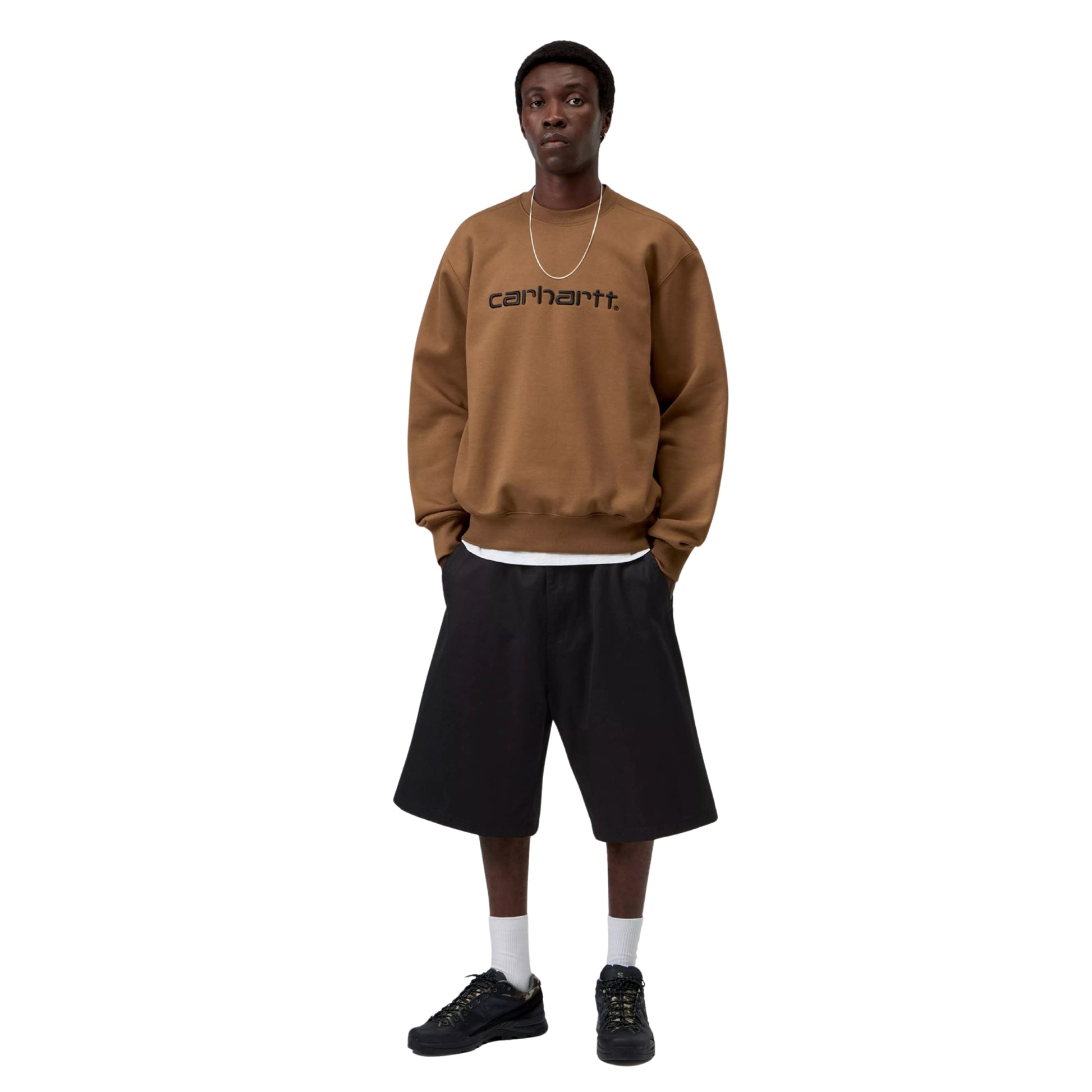 Sweatshirt Carhartt WIP Carhartt Sweat em WIP H Brown / Black — modelo masculino de frente, corpo inteiro, corrente fina prateada ao pescoço, logótipo Script "carhartt.®" bordado em Black no peito, calças largas pretas, meias brancas e sapatilhas pretas, malha escovada WIP H Brown, fundo branco.