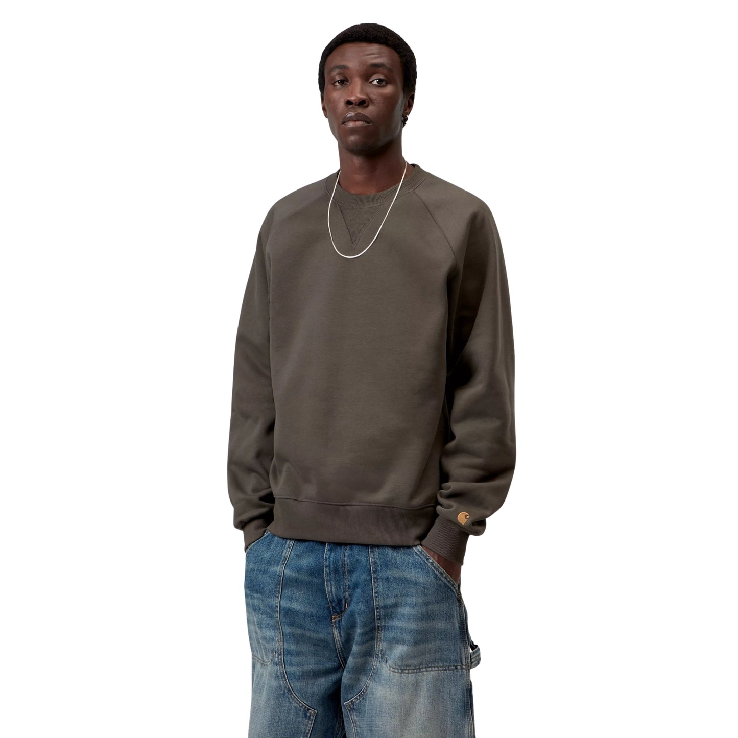 Sweat para homem Carhartt WIP Chase em Shungite / Gold — vista frontal com modelo, meio corpo, logo "C" dourado visível na manga esquerda, combinado com calças de ganga largas.