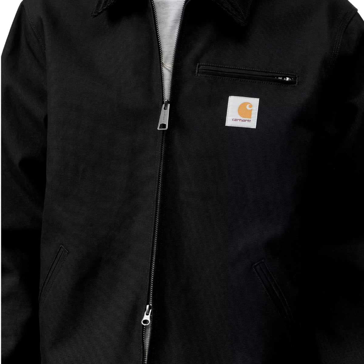 Pormenor do casaco Carhartt WIP Detroit preto com fecho frontal, bolso de peito com fecho e etiqueta do logótipo.