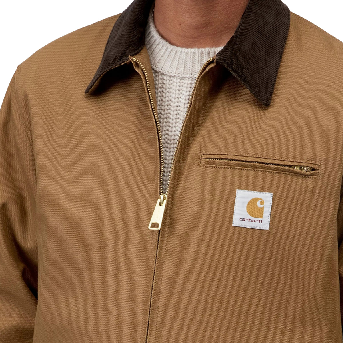 Casaco Carhartt WIP Detroit em Hamilton Brown/Tobacco Rigid, close-up da gola de bombazina escura, fecho metálico dourado, bolso de peito com fecho e etiqueta quadrada Carhartt.