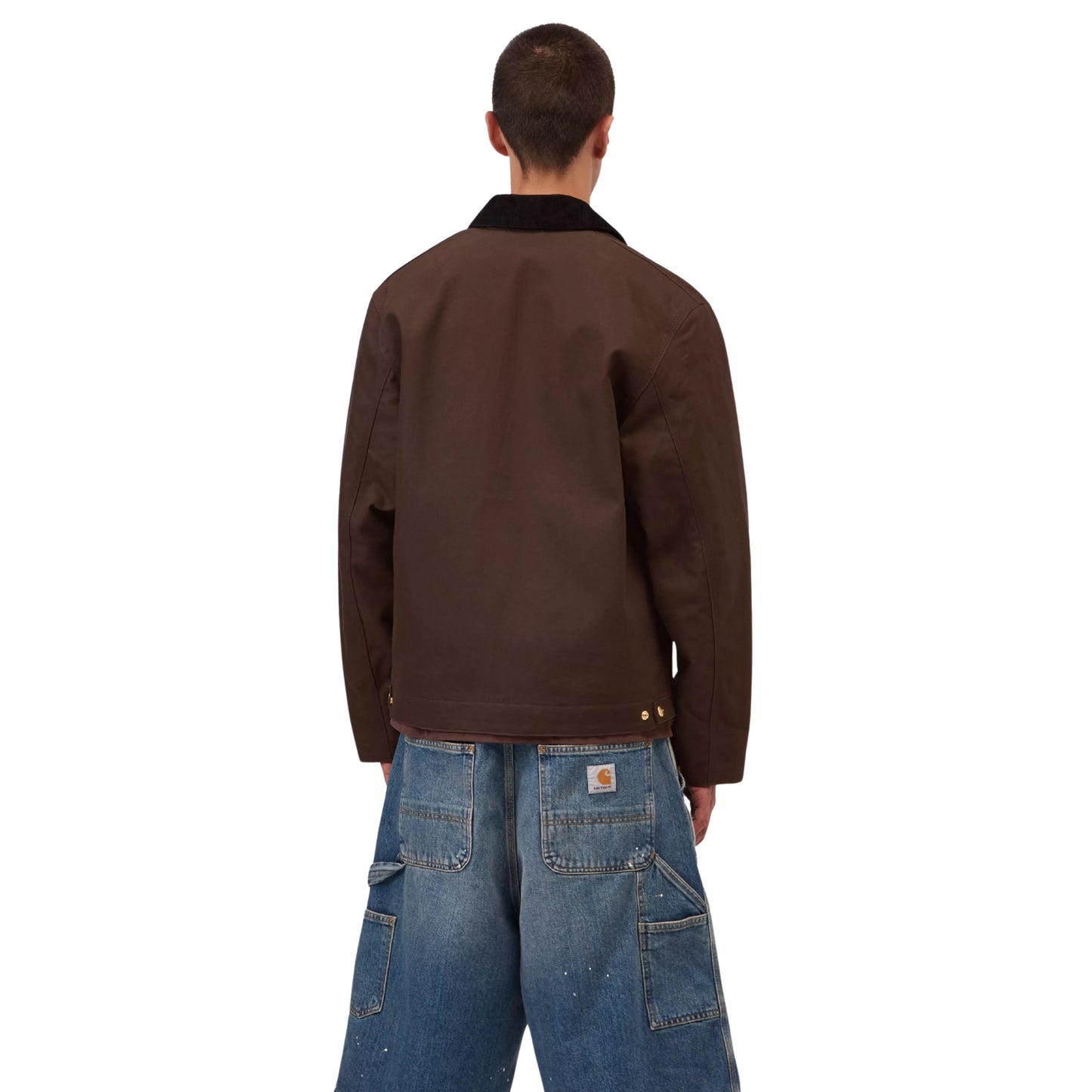 Casaco Carhartt WIP Detroit Jacket em Tobacco / Black Rigid — modelo masculino de costas, corpo inteiro, calças cargo denim largas azul-claro com patch Carhartt WIP nos bolsos traseiros, costas limpas em lona Dearborn Tobacco, rebites dourados na bainha e gola em bombazine preta visíveis, fundo branco.