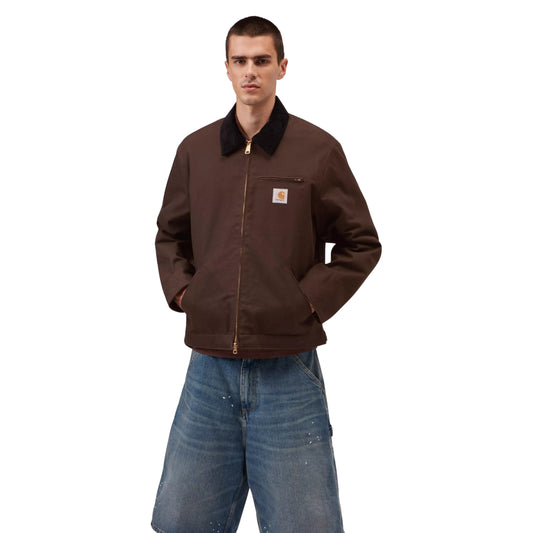 Casaco Carhartt WIP Detroit Jacket em Tobacco / Black Rigid — modelo masculino de frente, corpo inteiro, calças cargo denim largas azul-claro com respingos de tinta branca, mãos nos bolsos laterais com debrum, corte solto e quadrado visível, fundo branco.