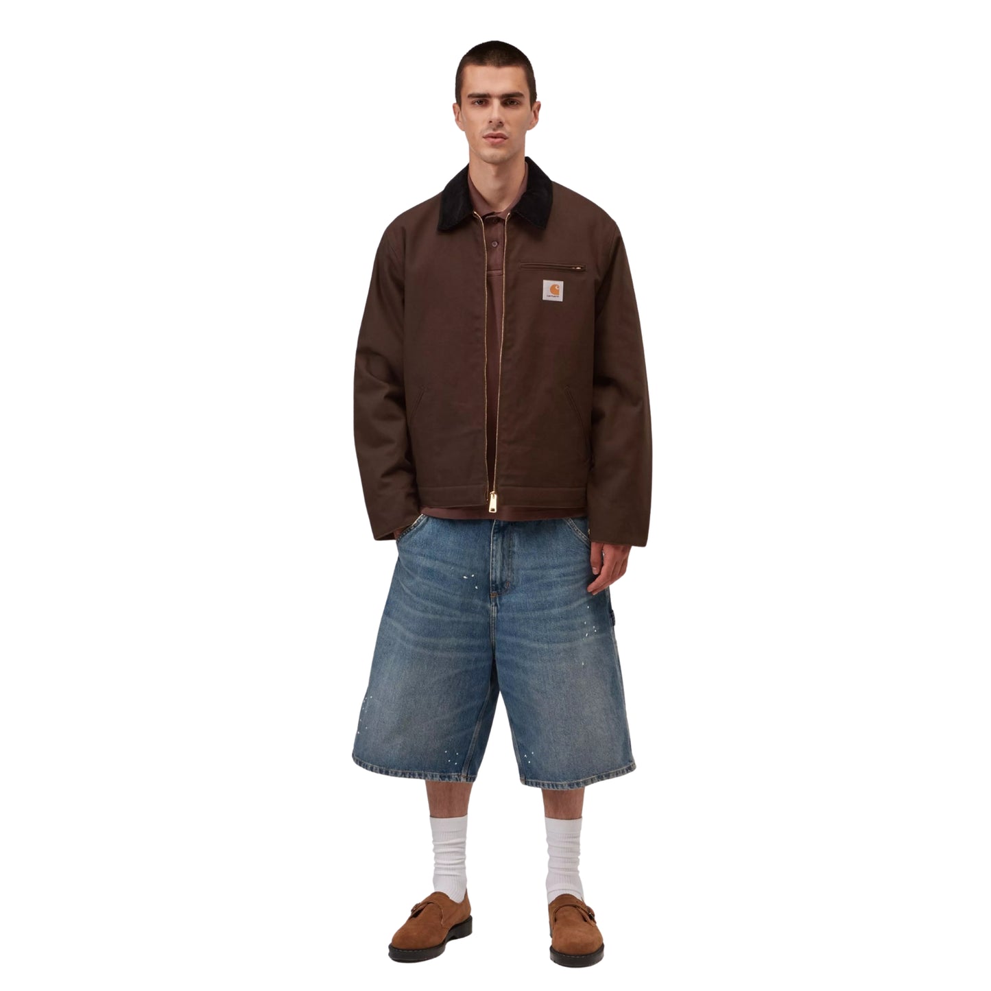 Casaco Carhartt WIP Detroit Jacket em Tobacco / Black Rigid — modelo masculino de frente, corpo inteiro, calças cargo denim largas azul-claro com respingos de tinta branca, meias brancas altas e mocassins castanhos, casaco aberto a revelar polo castanho escuro por baixo, fundo branco.