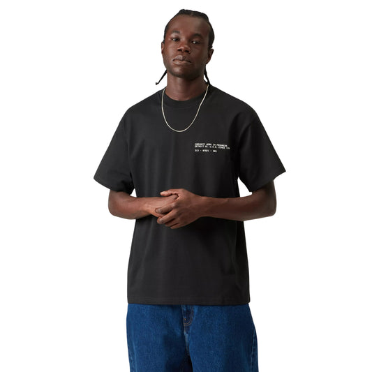 T-shirt Carhartt WIP S/S Feather Progress em Black — modelo masculino de frente, meio corpo superior, cabelo com tranças apanhadas, fio prateado ao pescoço, anel dourado, t-shirt preta de algodão orgânico com corte solto e print de texto branco discreto no peito esquerdo, calças wide-leg em ganga azul, fundo branco.