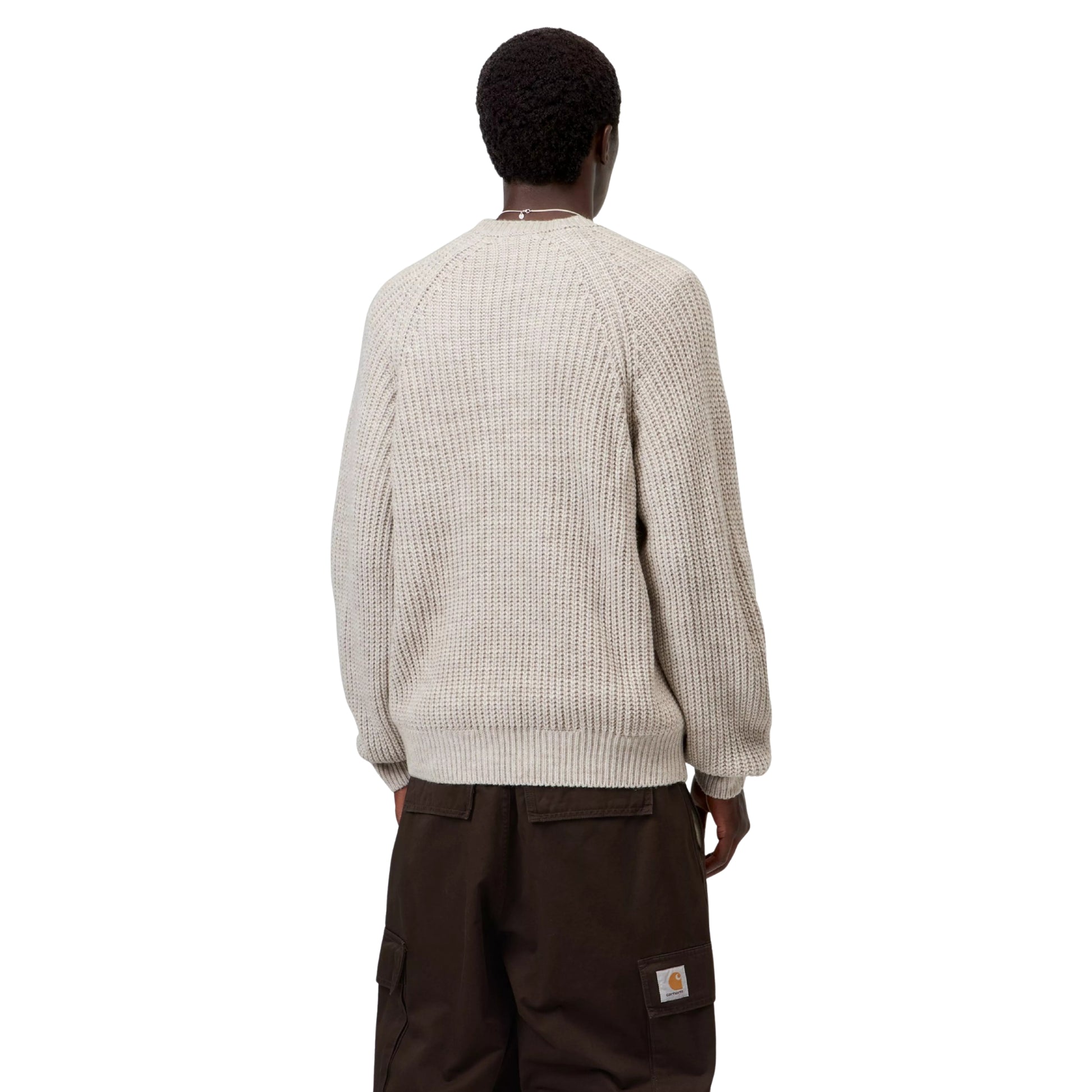 Camisola Carhartt WIP Firth Sweater em Fleur de Sel — modelo a usar a camisola de costas,meio corpo visivel, malha bege-areia muito claro com textura canelada vertical, mangas raglan, decote redondo, punhos e bainha canelados, calças cargo castanho-escuras com Square Label Carhartt WIP visível, fundo branco.