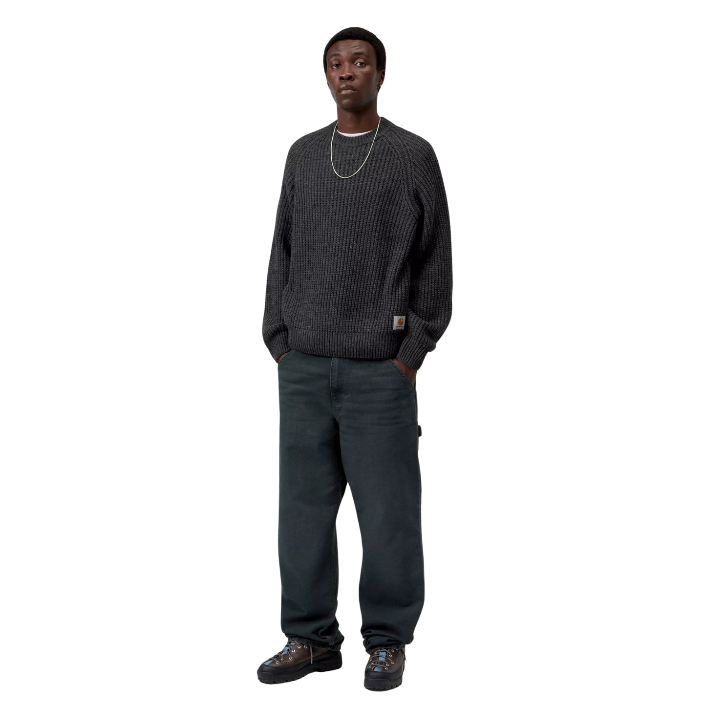 Camisola Carhartt WIP Firth Sweater em Soot — modelo a usar a camisola de frente, corpo inteiro, malha cinzento-chumbo escuro com textura canelada vertical, mangas raglan, decote redondo, etiqueta Square Label Carhartt WIP na bainha, calças cargo cinzento-escuras e botas pretas, fundo branco.