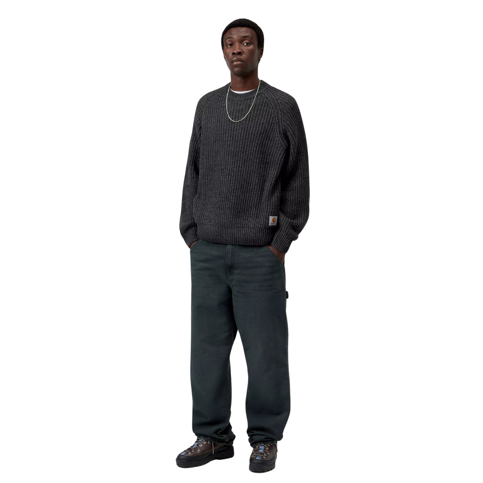 Camisola Carhartt WIP Firth Sweater em Soot — modelo a usar a camisola de frente, corpo inteiro, malha cinzento-chumbo escuro com textura canelada vertical, mangas raglan, decote redondo, etiqueta Square Label Carhartt WIP na bainha, calças cargo cinzento-escuras e botas pretas, fundo branco.