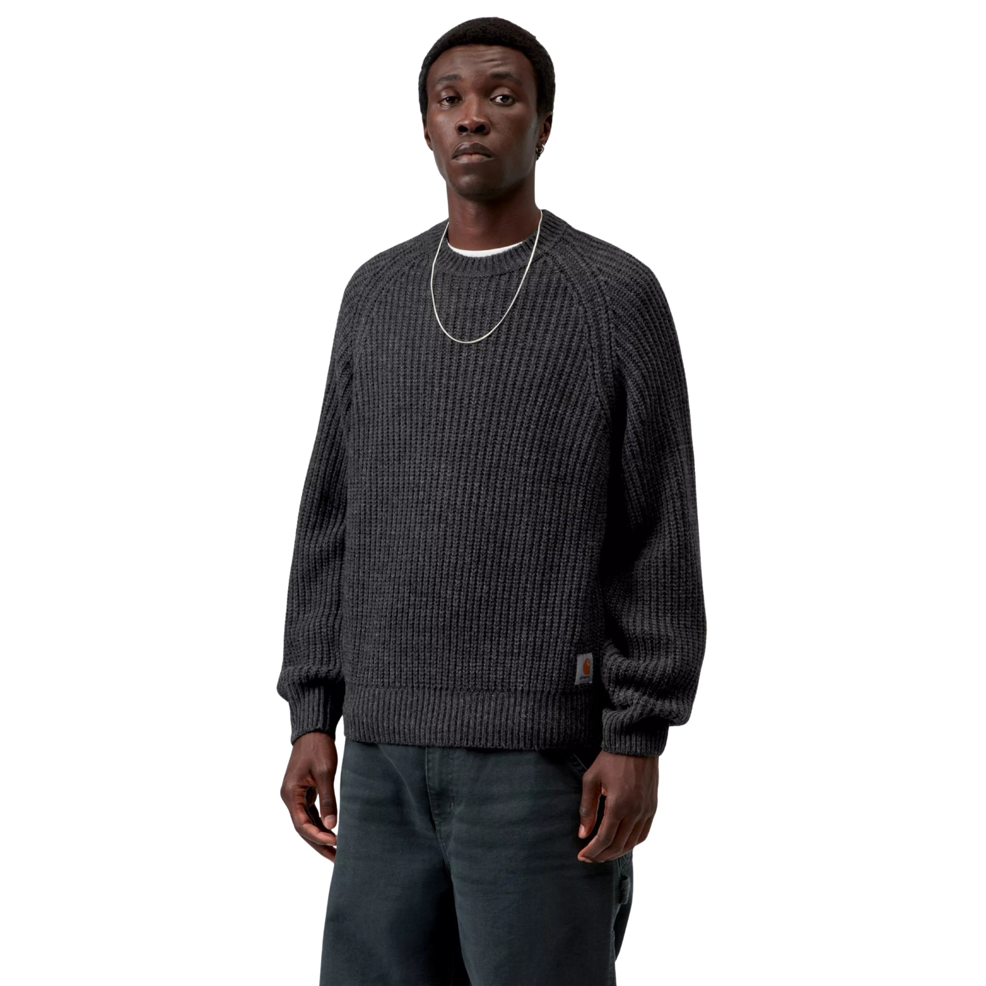 Camisola Carhartt WIP Firth Sweater em Soot — modelo a usar a camisola de frente, meio corpo superior, malha cinzento-chumbo escuro com textura canelada vertical, mangas raglan, decote redondo, etiqueta Square Label Carhartt WIP na bainha inferior direita e corrente prateada ao pescoço, fundo branco.