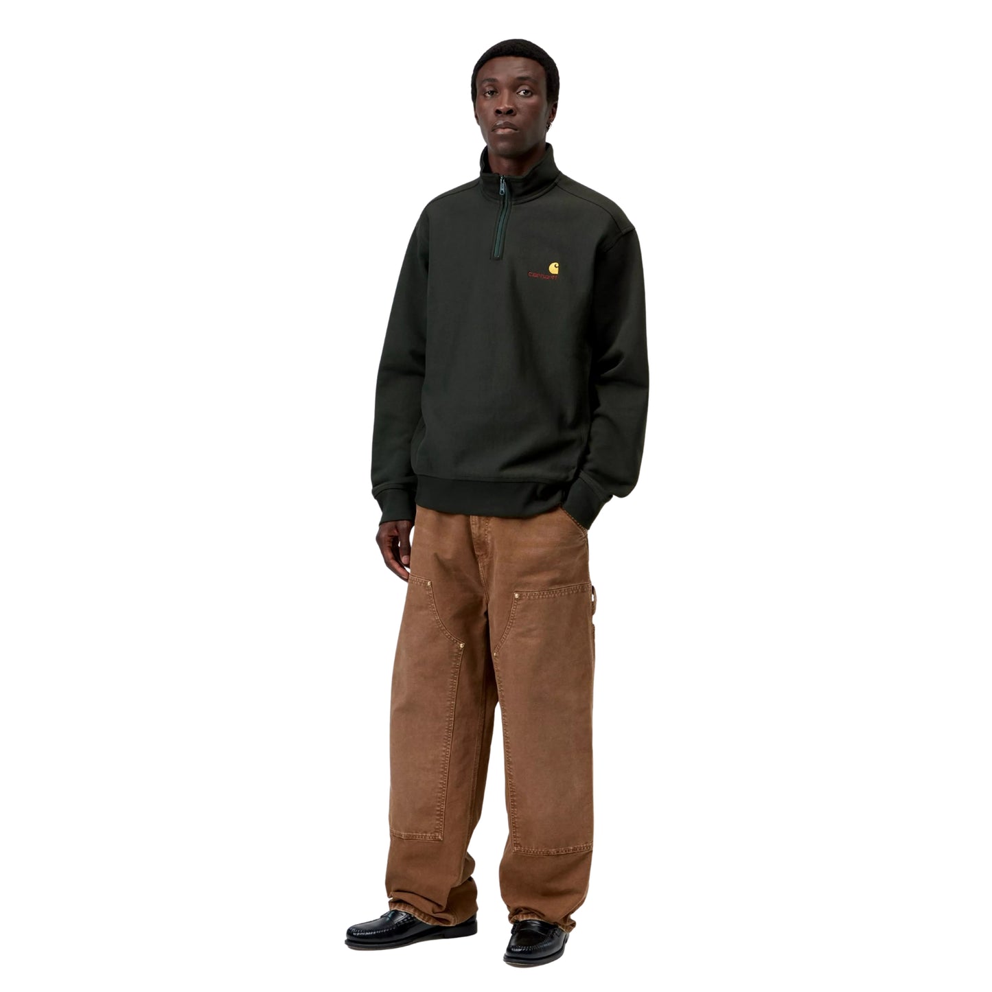 Sweatshirt Carhartt WIP Half Zip American Script em Raven — modelo a usar a peça de frente, corpo inteiro, gola alta com fecho de correr, bordado American Script com logótipo C amarelo no peito esquerdo, calças Double Knee em castanho Hamilton Brown desgastado e mocassins pretos, fundo branco.