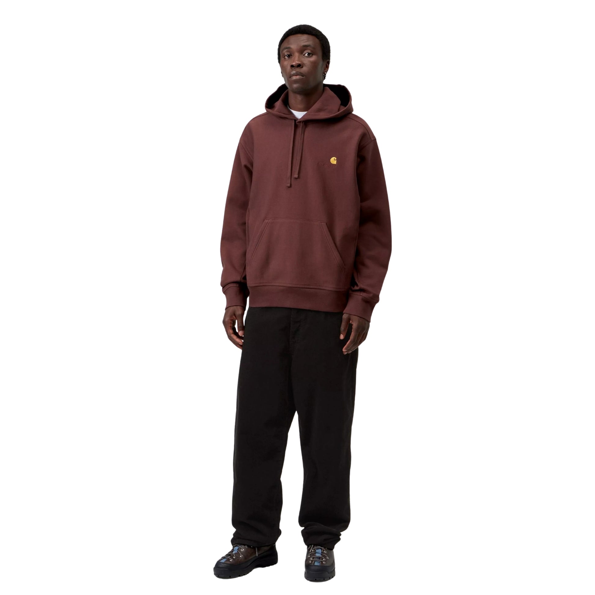 Hoodie Carhartt WIP Hooded American Script Sweat em Amarone — modelo a usar a peça de frente, corpo inteiro, capuz com cordão duplo, bolso canguru, logótipo C amarelo-dourado com texto carhartt em tom-sobre-tom no peito esquerdo, calças wide-leg pretas e botas de caminhada pretas, fundo branco.