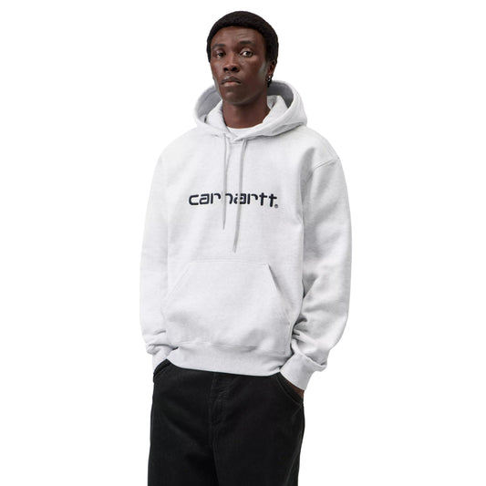 Hoodie Carhartt WIP Hooded Carhartt Sweat em Ash Heather — modelo masculino de frente, meio corpo, cabelo curto escuro, brinco pequeno na orelha direita, capuz levantado com interior cinzento Graphite visível, cordão de ajuste cinzento com ponteiras metálicas, logótipo Script "carhartt.®" bordado ao peito em Graphite, bolso canguru com mãos dentro, punhos canelados, calças wide-leg pretas Carhartt WIP, malha escovada cinzento mesclado Ash Heather, fundo branco.