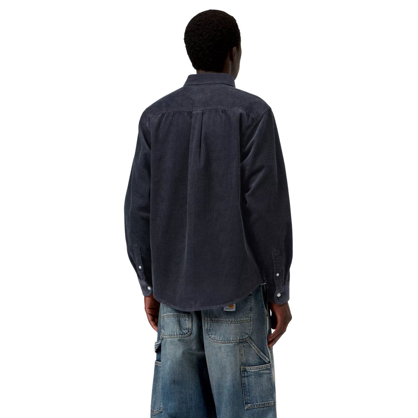 Camisa Carhartt WIP L/S Madison Cord Shirt em Dark Navy — modelo masculino de costas, meio corpo superior, cabelo curto, camisa de bombazina azul-marinho escuro com corte regular, colarinho button-down, pala central nas costas, canelado largo visível, botões brancos nos punhos, calças wide-leg denim azul-claro Double Knee com Square Label Carhartt WIP e desgaste visíveis, fundo branco.