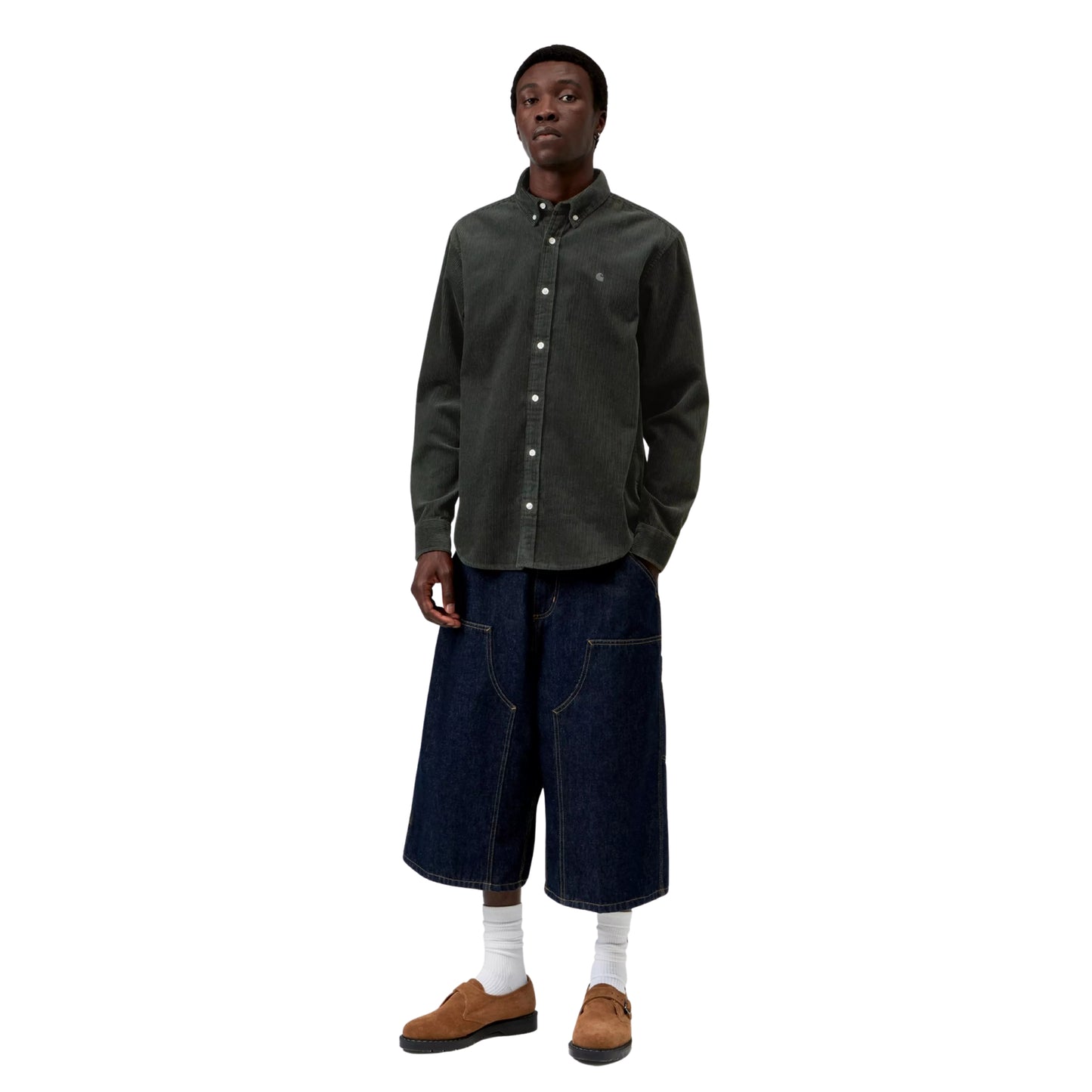 Camisa Carhartt WIP L/S Madison Cord Shirt em Raven — modelo masculino de frente, corpo inteiro, cabelo preto curto afro, camisa de bombazina verde-floresta muito escuro com corte regular, colarinho button-down, botões brancos, logótipo "C" bordado em tom-sobre-tom no peito esquerdo, calças wide-leg carpenter denim azul-escuro com costuras contrastantes brancas Carhartt WIP, meias brancas altas, sapatos derby em camurça castanha, fundo branco.