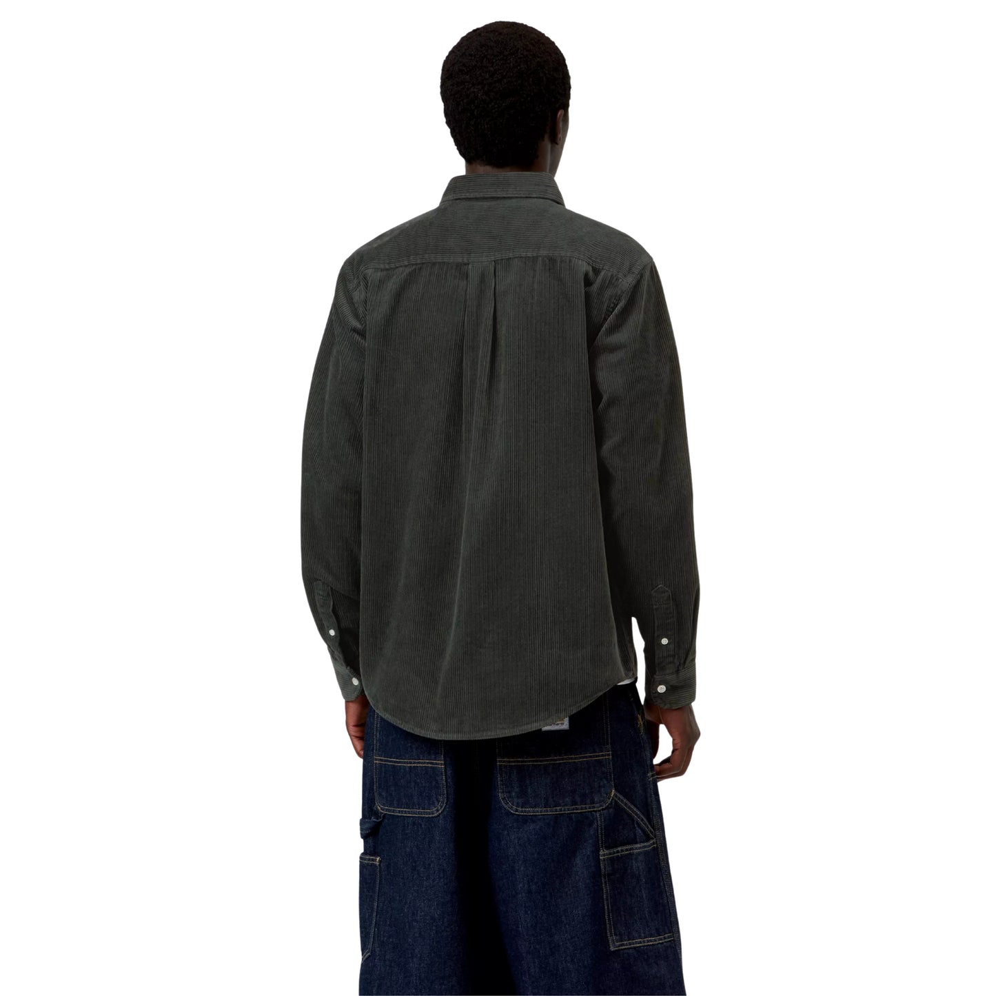 Camisa Carhartt WIP L/S Madison Cord Shirt em Raven — modelo masculino de costas, corpo inteiro, cabelo preto curto afro, camisa de bombazina verde-floresta muito escuro com corte regular, pala central nas costas, canelado largo, botões prateados nos punhos, calças wide-leg carpenter denim azul-escuro com costuras contrastantes brancas Carhartt WIP, meias brancas altas, sapatos derby em camurça castanha, fundo branco.