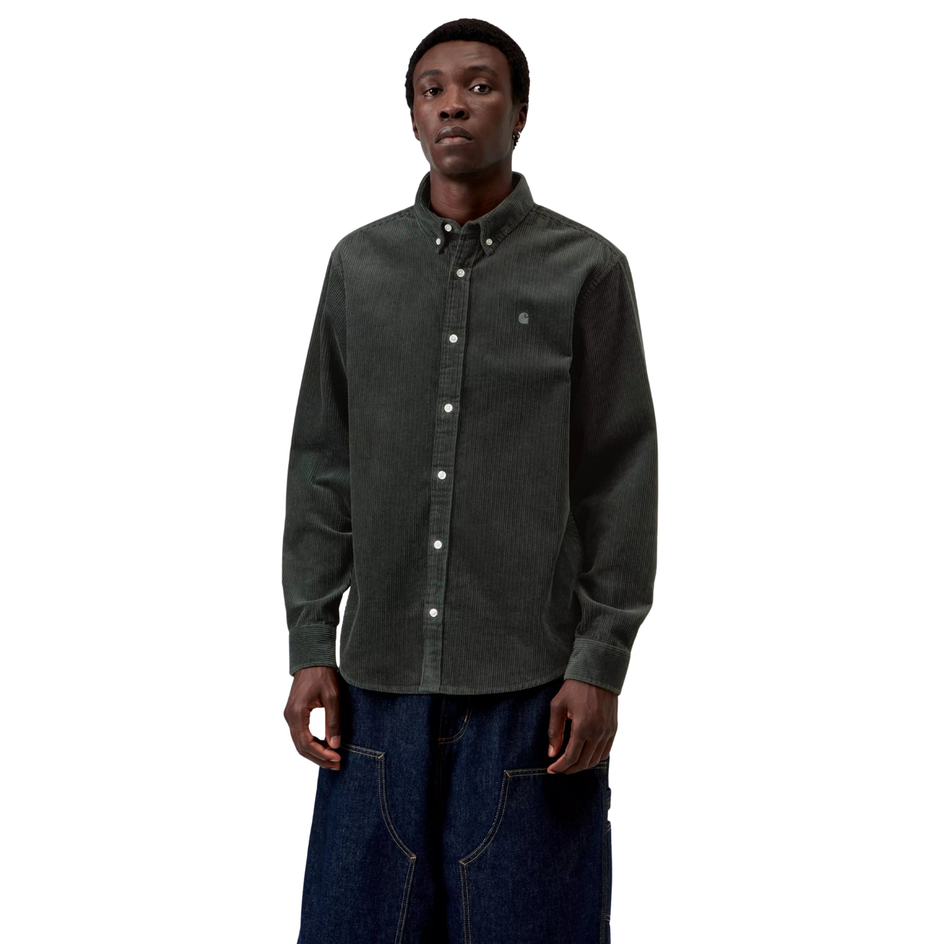 Camisa Carhartt WIP L/S Madison Cord Shirt em Raven — modelo masculino de frente, meio corpo superior, cabelo preto curto afro, brinco pequeno, camisa de bombazina verde-floresta muito escuro com corte regular e logótipo "C" Carhartt bordado em tom-sobre-tom no peito esquerdo em destaque, colarinho button-down, botões brancos, calças wide-leg carpenter denim azul-escuro, fundo branco.