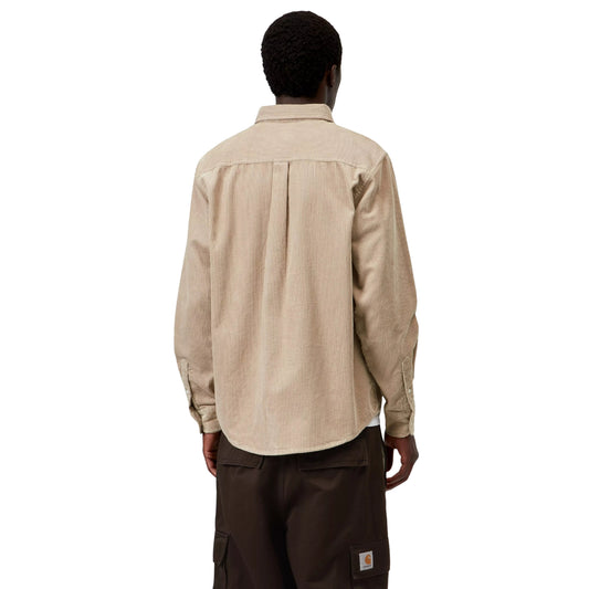 Camisa Carhartt WIP L/S Madison Cord Shirt em Wall — modelo masculino de costas, meio corpo superior e inferior, cabelo curto preto, camisa de bombazina bege-areia com corte regular, pala central nas costas, canelado largo, punho com botão, barra curva, calças cargo wide-leg castanho-escuro com Square Label Carhartt WIP dourado visível no bolso traseiro, fundo branco.