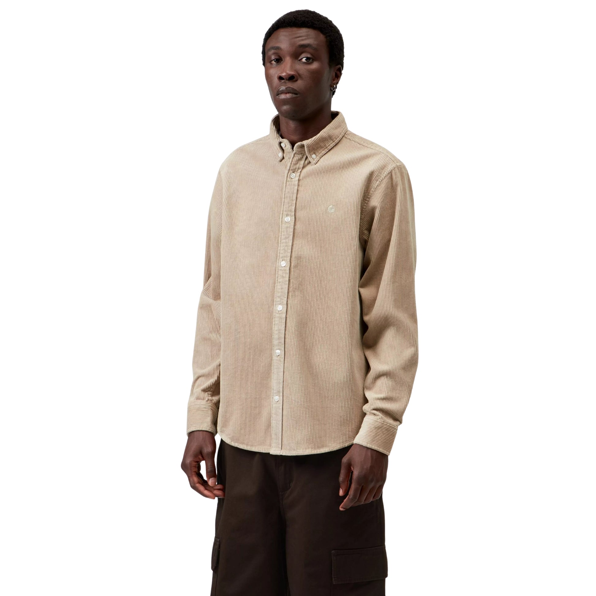 Camisa Carhartt WIP L/S Madison Cord Shirt em Wall — modelo masculino de frente, meio corpo superior, cabelo curto preto, brinco pequeno, camisa de bombazina bege-areia com colarinho button-down, fecho com botões brancos, logótipo "C" Carhartt bordado em tom-sobre-tom no peito esquerdo em destaque, canelado largo da bombazina visível, calças cargo castanho-escuro, fundo branco.