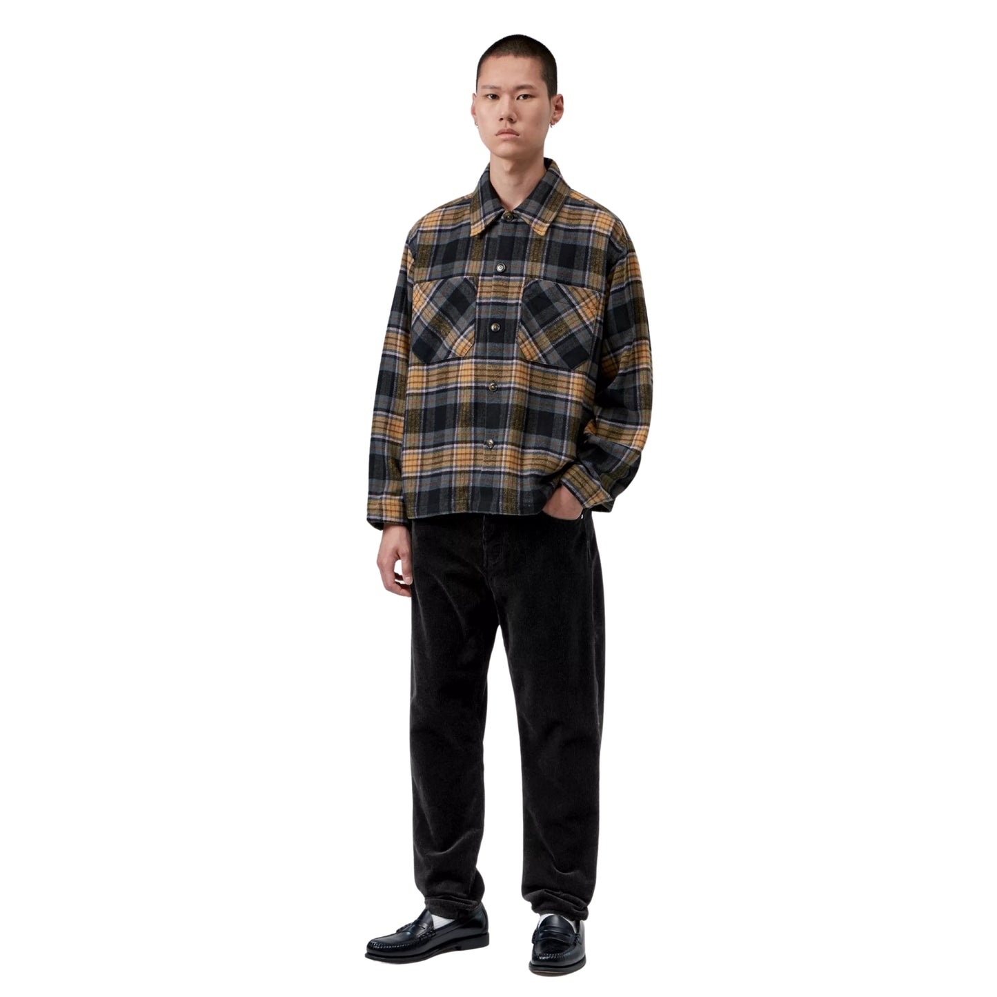 Calças Carhartt WIP Newel Pant em Black — modelo masculino asiático de corpo inteiro, cabelo curto preto, casaco xadrez oversized castanho e cinzento Carhartt WIP, calças em bombazina preta com corte relaxado afunilado a empilhar ligeiramente nas sapatilhas, loafers pretos de bico redondo com meias brancas visíveis, fundo branco.