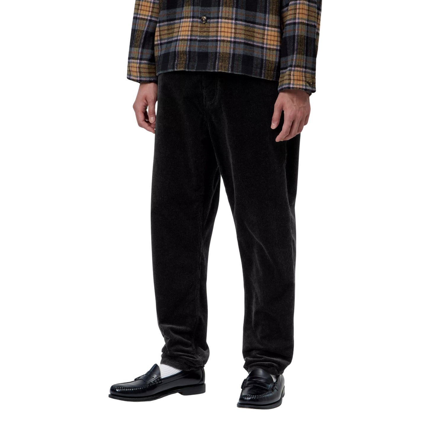 alças Carhartt WIP Newel Pant em Black — modelo masculino de frente, corpo inteiro sem cabeça, casaco xadrez oversized Carhartt WIP, calças em bombazina Coventry preta com corte relaxado afunilado e perna larga a afunilar no tornozelo, loafers pretos com meias brancas, fundo branco.