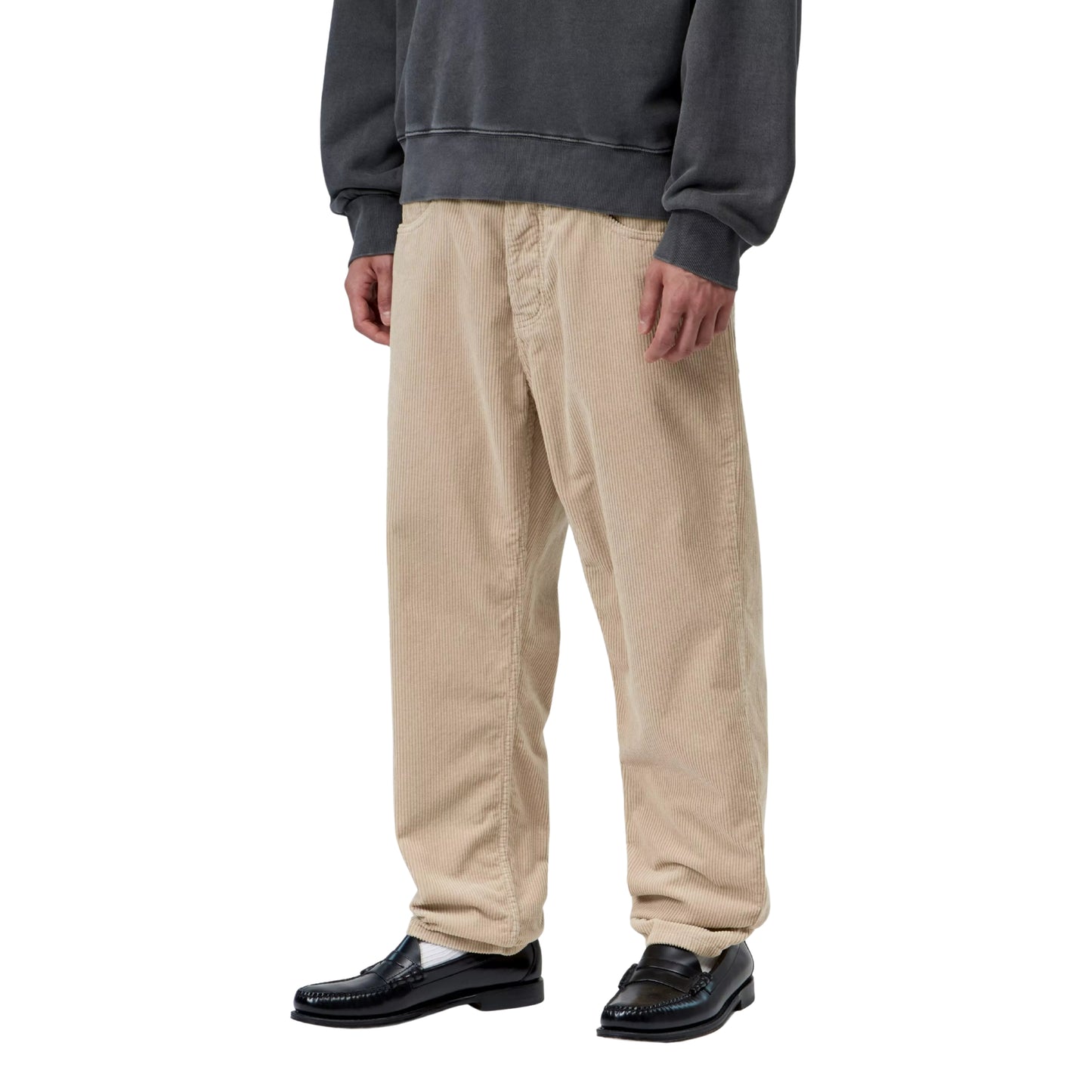 Calças Carhartt WIP Newel Pant em Wall Rinsed — modelo masculino de frente a 3/4, meio corpo inferior, sweatshirt oversized cinzenta escura Carhartt WIP, calças em bombazina Coventry bege Wall rinsed com corte relaxado afunilado e cintura regular, bolsos frontais com rebites prateados visíveis, loafers pretos, fundo branco.