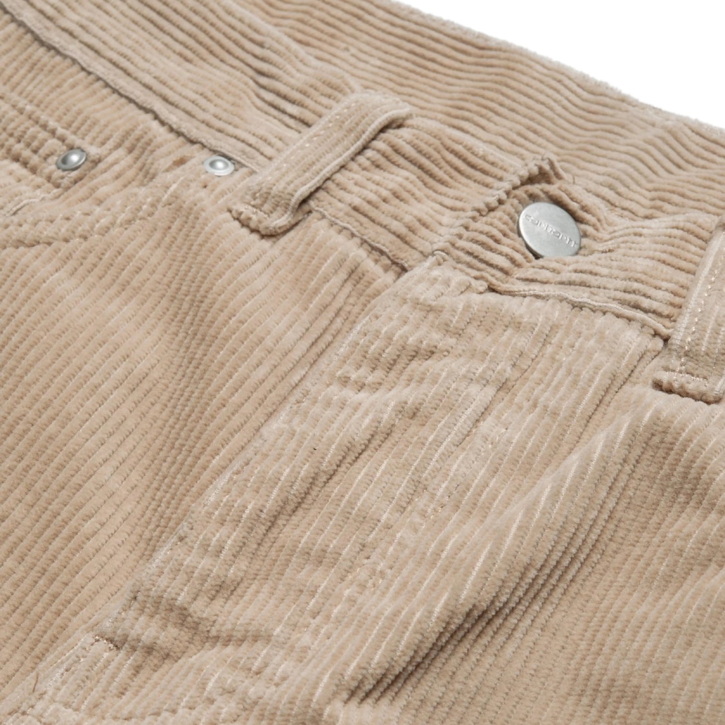 Calças Carhartt WIP Newel Pant em Wall Rinsed — detalhe da cintura frontal em close, bombazina Coventry de oito nervuras bege Wall rinsed, botão metálico prateado com gravação Carhartt, rebites prateados nos bolsos frontais e micro-bolso, textura canelada larga e lavagem rinsed em destaque, fundo branco.