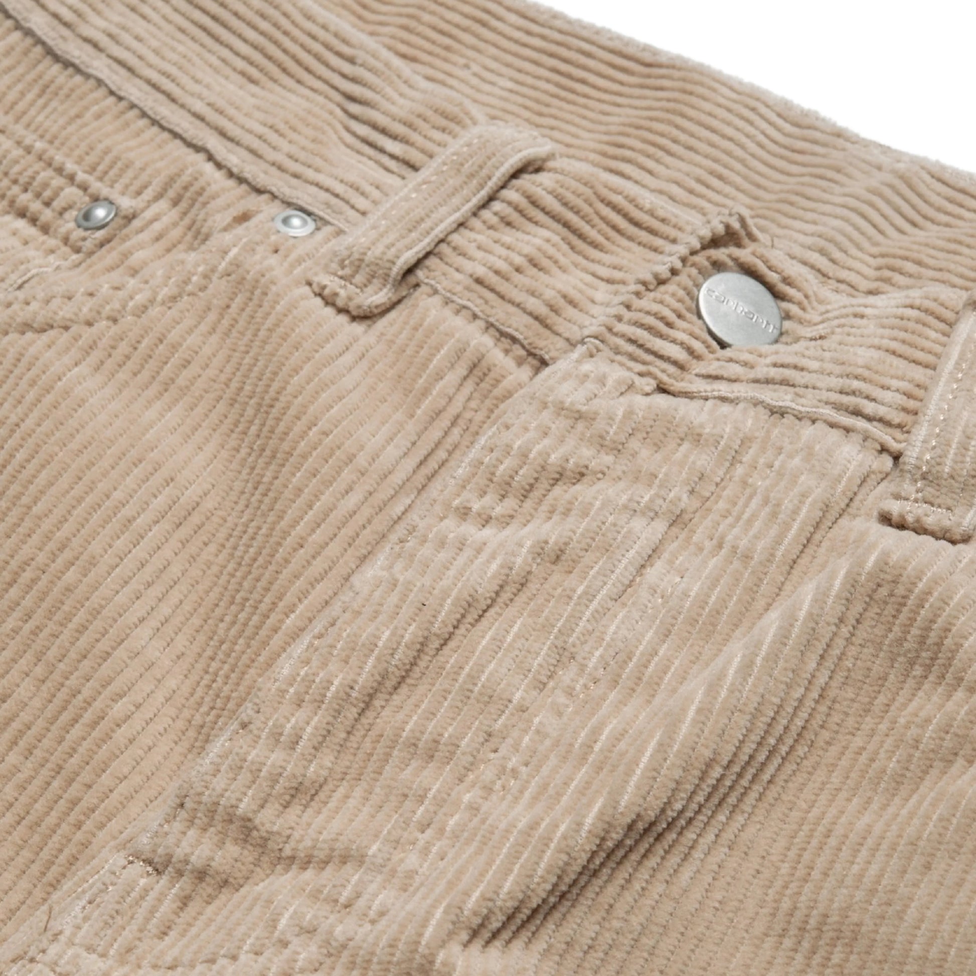 Calças Carhartt WIP Newel Pant em Wall Rinsed — detalhe da cintura frontal em close, bombazina Coventry de oito nervuras bege Wall rinsed, botão metálico prateado com gravação Carhartt, rebites prateados nos bolsos frontais e micro-bolso, textura canelada larga e lavagem rinsed em destaque, fundo branco.