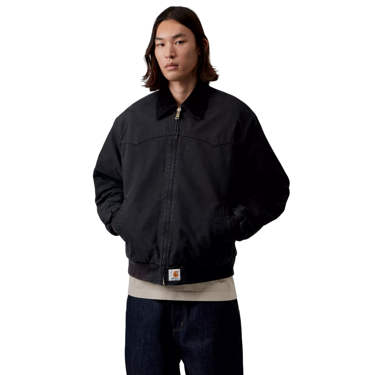 Casaco Carhartt WIP OG Santa Fe em Preto — modelo masculino de frente, meio corpo, fecho de correr dourado fechado, gola em bombazine preta, Square Label Carhartt WIP na bainha, punhos canelados pretos, corte Loose OG oversized, sweatshirt bege por baixo, fundo branco.